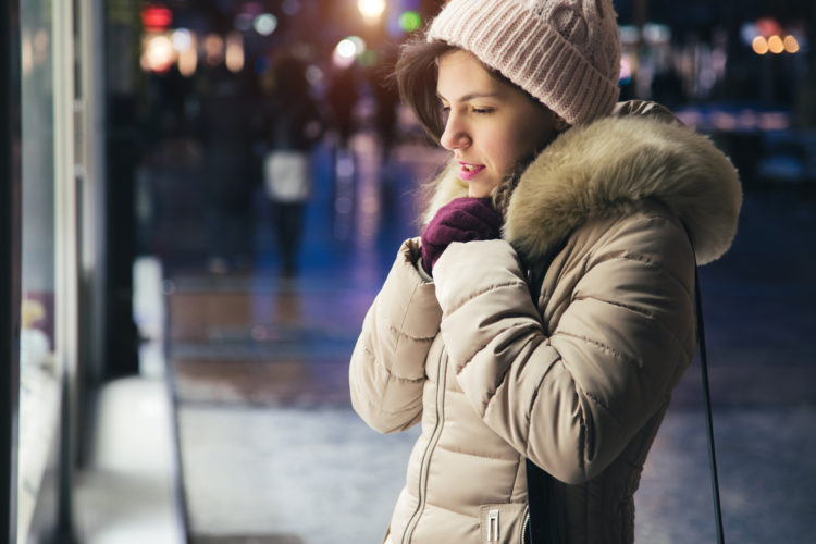 Young brunette woman standing in front of store window and freezing