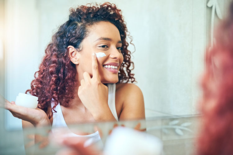 Attractive young woman applying moisturizer to her face