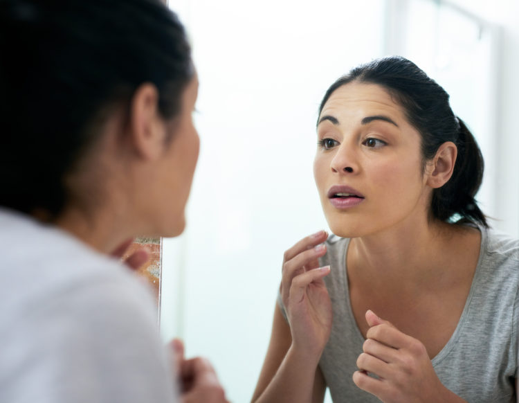 Rearview shot of a young woman examining her face in the bathroom mirror