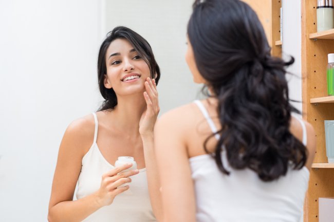 Young women applying cream looking into mirror