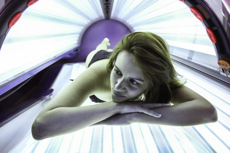 Young beautiful woman lying on a tanning bed in a solarium. About 25 years old, Caucasian female in black bikini.