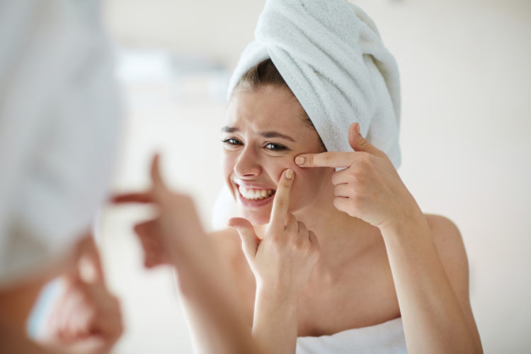Displeased young woman squeezing pimples in front of mirror