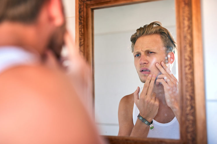 young man examining his skin in the bathroom mirror