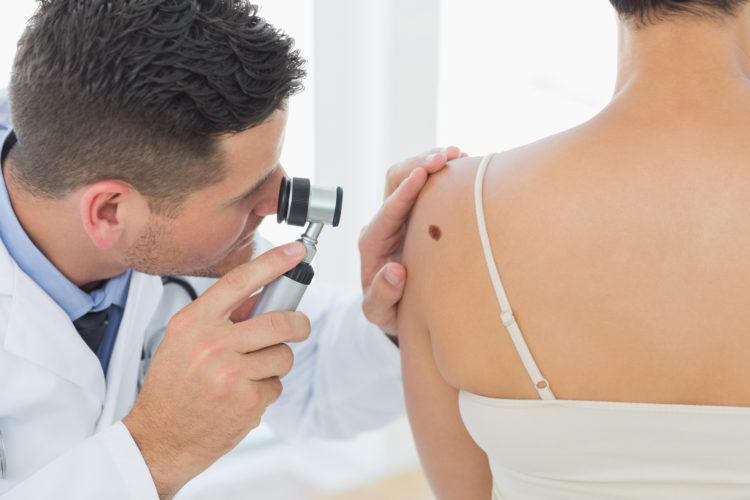Doctor examining mole on back of woman in clinic
