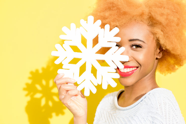 Portrait of a cute african woman in blue sweater holding an artificial snowflake on the yellow background