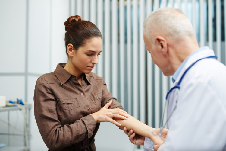 Young sick woman showing her arm to doctor while visiting clinics