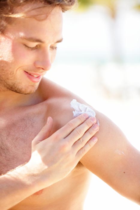 Handsome man applying sunscreen on his shoulder