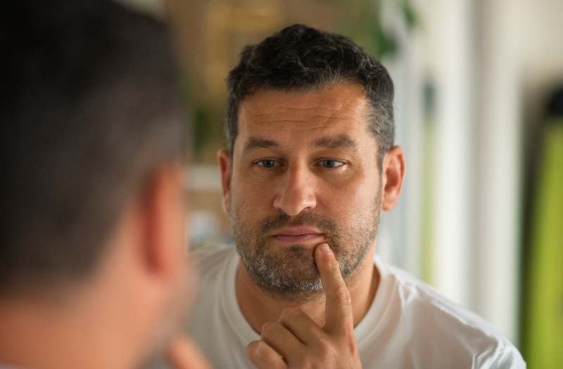 A man touches his lip where a cold sore is by Swinyer Woseth Dermatology