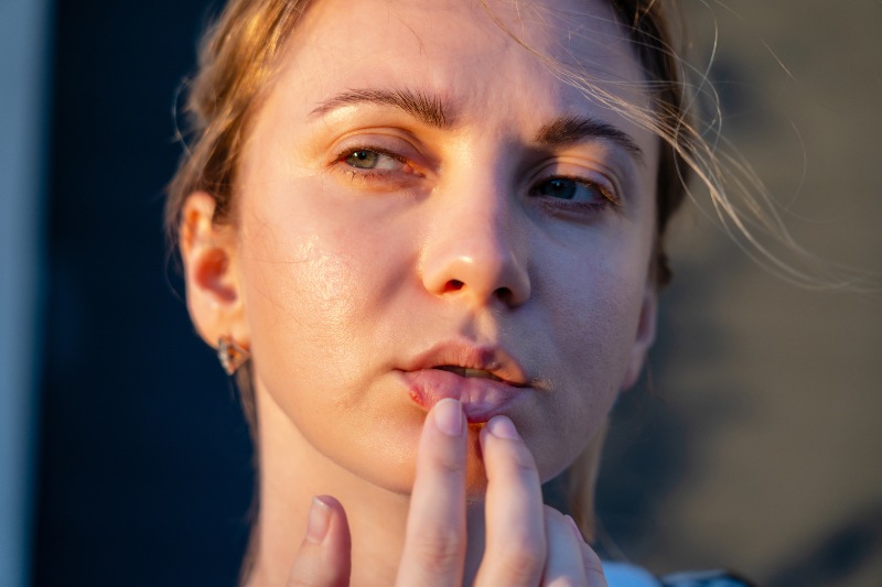 A woman touching her bottom lip with a cold sore on it by Swinyer Woseth Dermatology