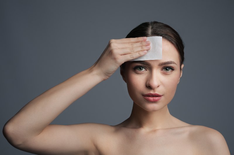 A woman using a mattifying wipe on her forehead by Swinyer Woseth Dermatology