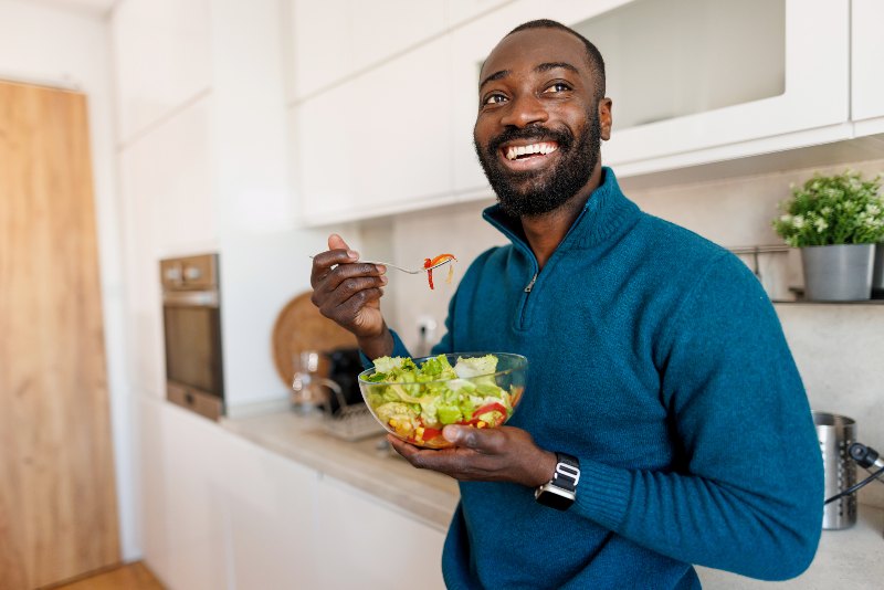 A smiling man eating a bowl of salad by Swinyer Woseth Dermatology