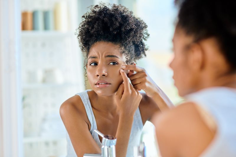 A woman with hormonal acne looking in a mirror by Swinyer Woseth Dermatology