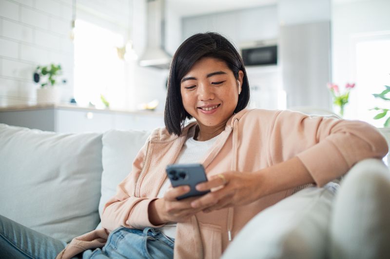 A woman smiling while looking down at her phone with blue light by Swinyer Woseth Dermatology